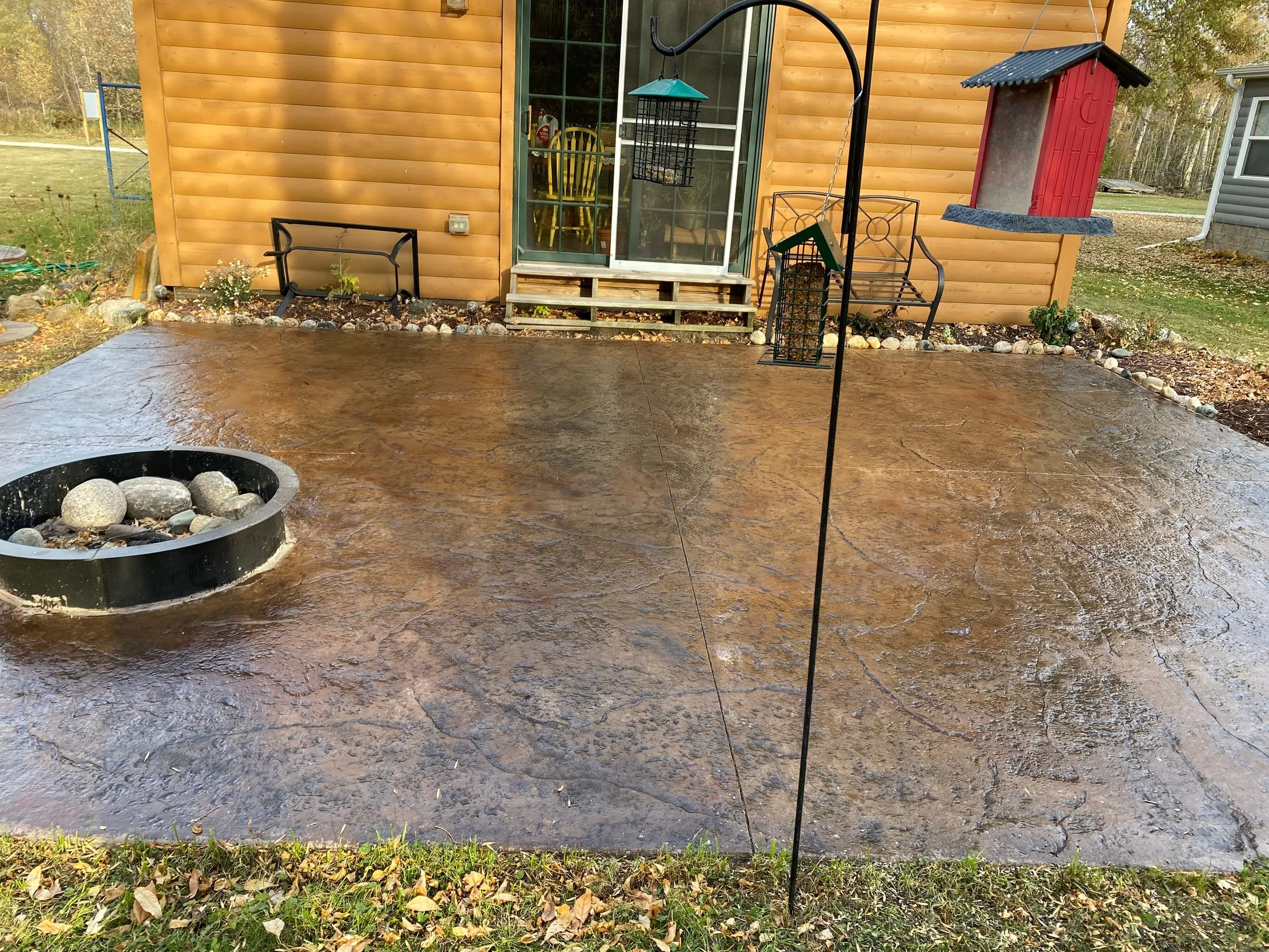 Stamped concrete patio with integral color and a built-in fire pit beside a log-sided home.