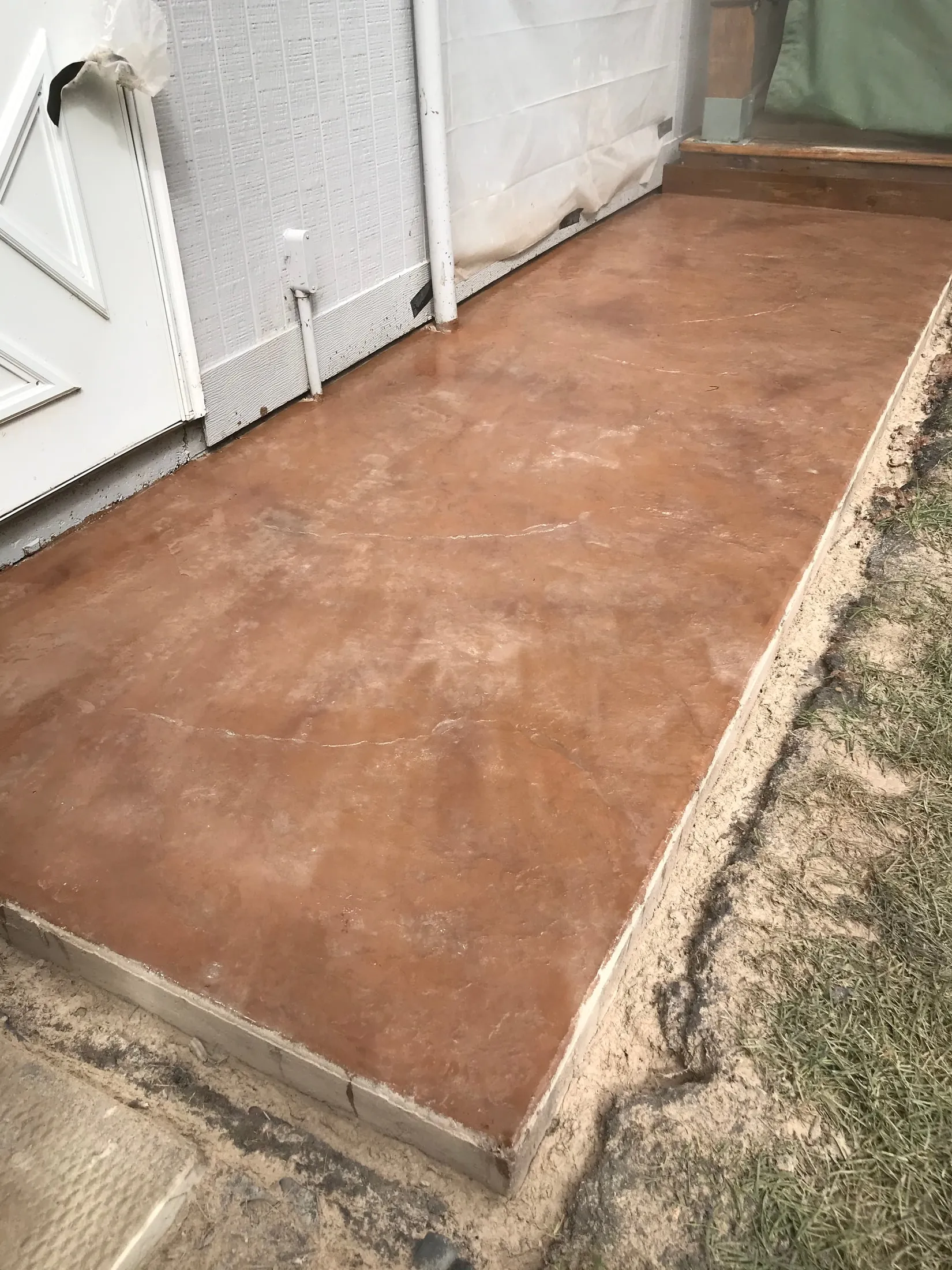 Concrete entry slab in warm brown integral color beside a door.