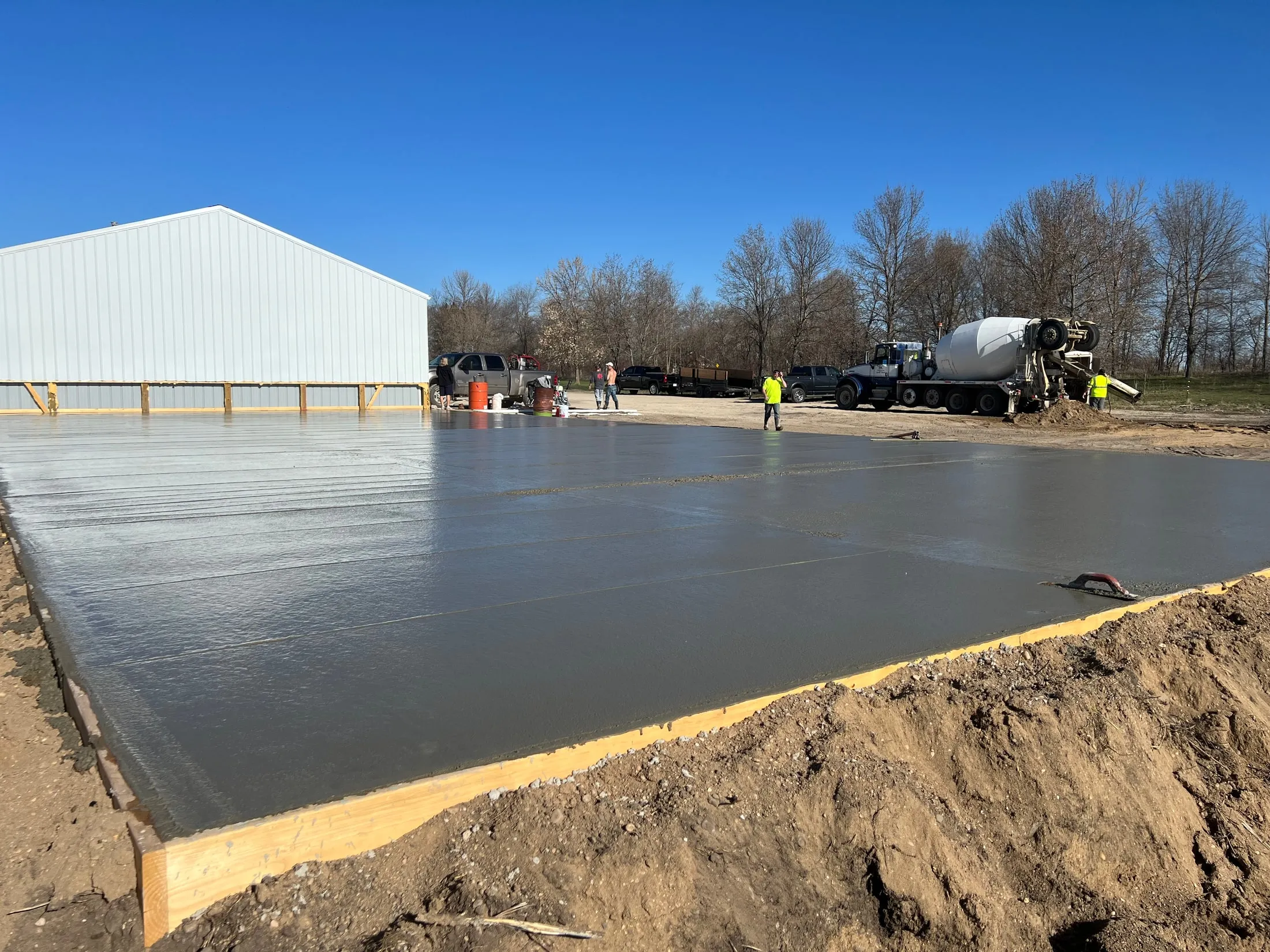 Wide view of a large concrete slab during finishing beside a metal building.