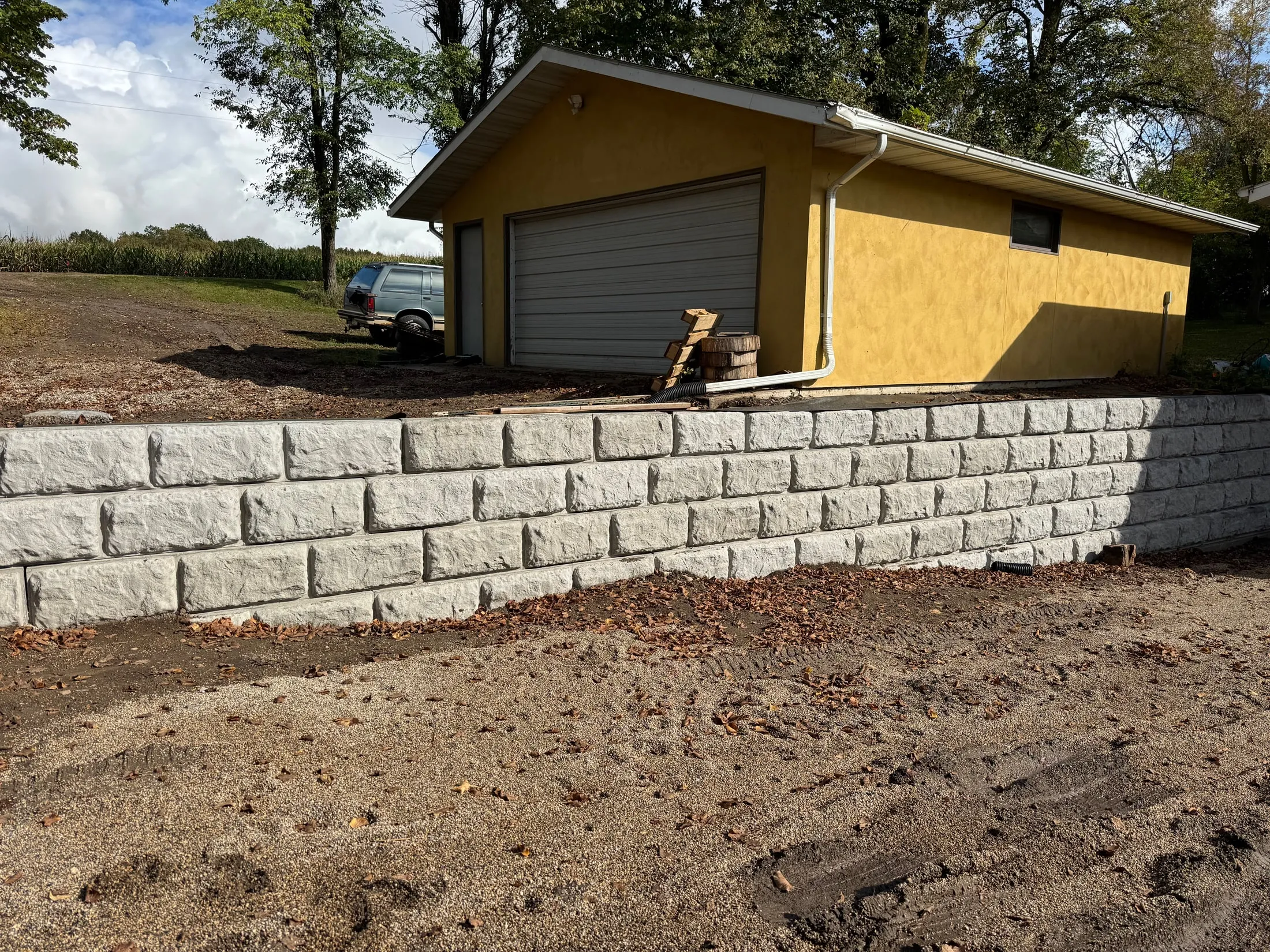 Gray block retaining wall beside a garage with exposed soil.