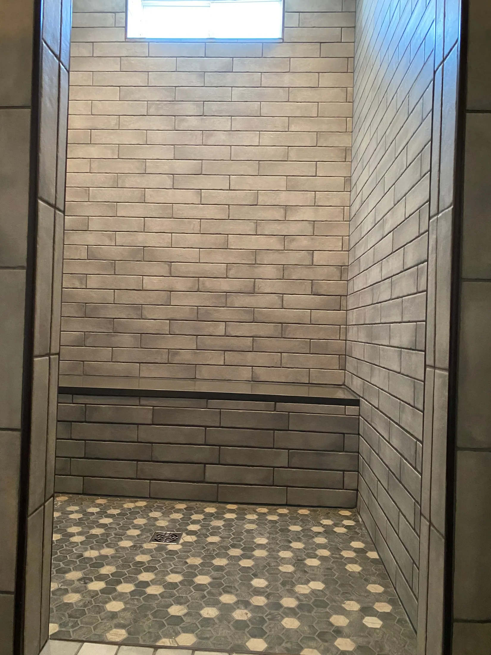 Gray subway tile walls with hex mosaic floor in the walk-in shower.
