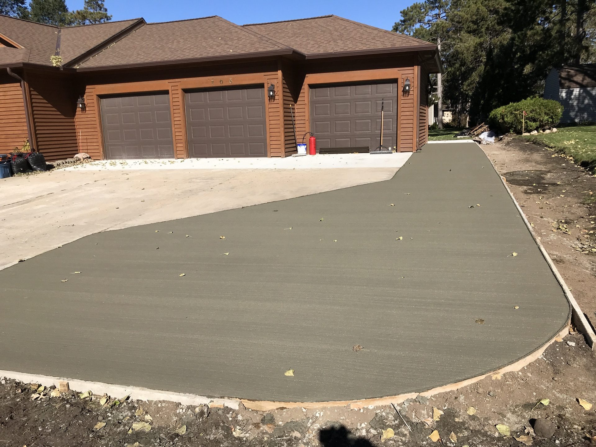 Newly poured concrete driveway with curved edge adjoining an existing paved area, brick home with three-car garage in background.