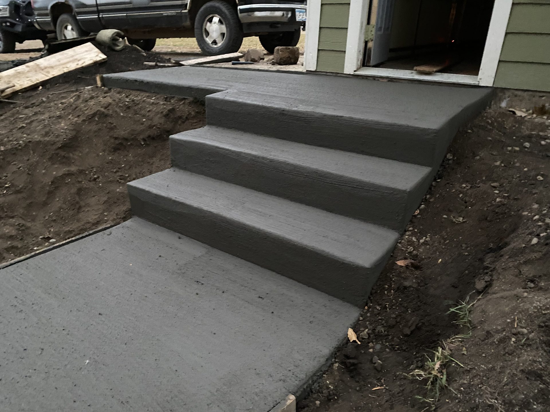Newly installed concrete steps leading to a garage entrance, showing four finished treads with clean edges and proper grading.