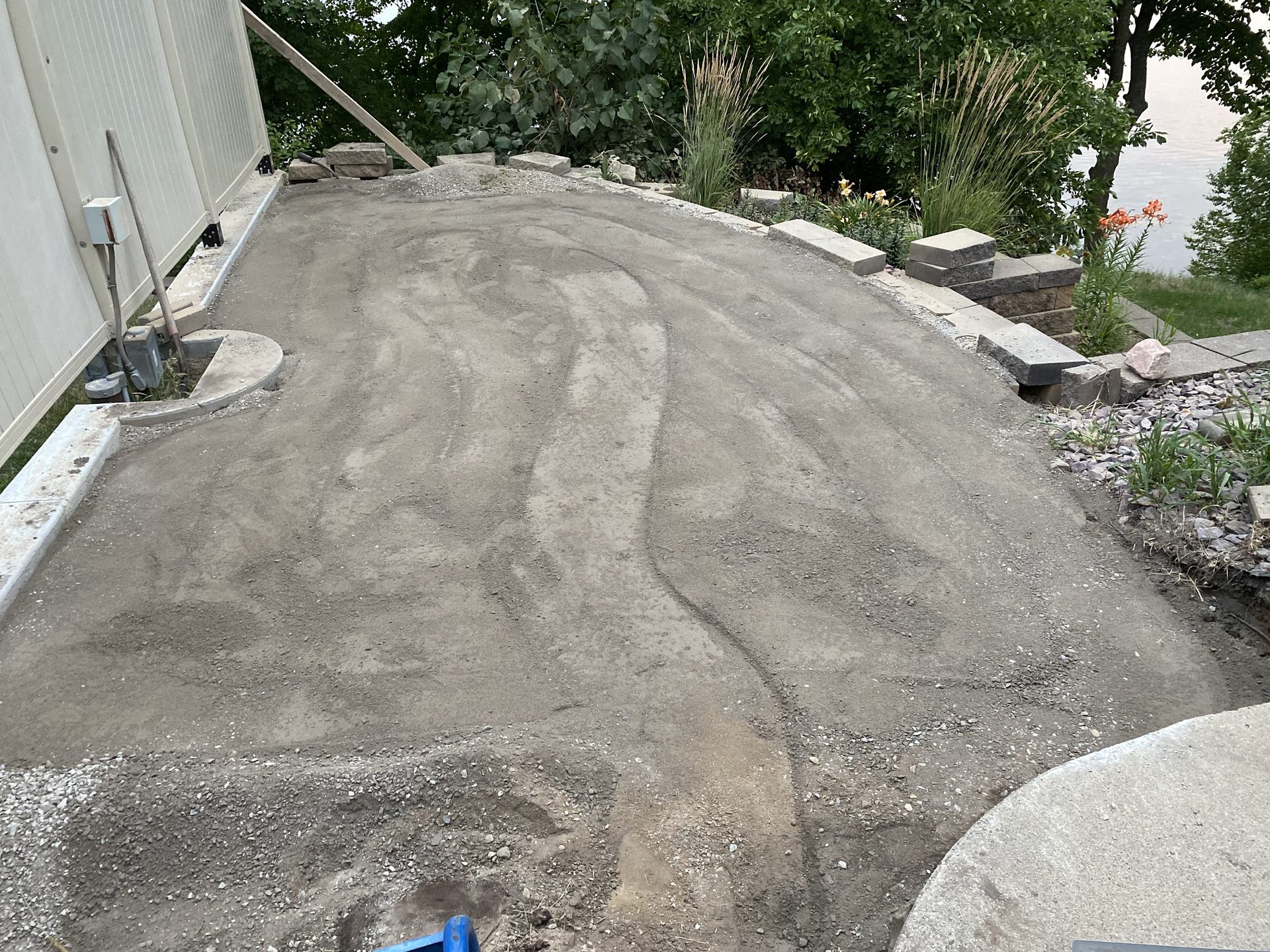 Freshly graded gravel base base showing grade lines and preparation work, with landscape borders and retaining wall elements visible.