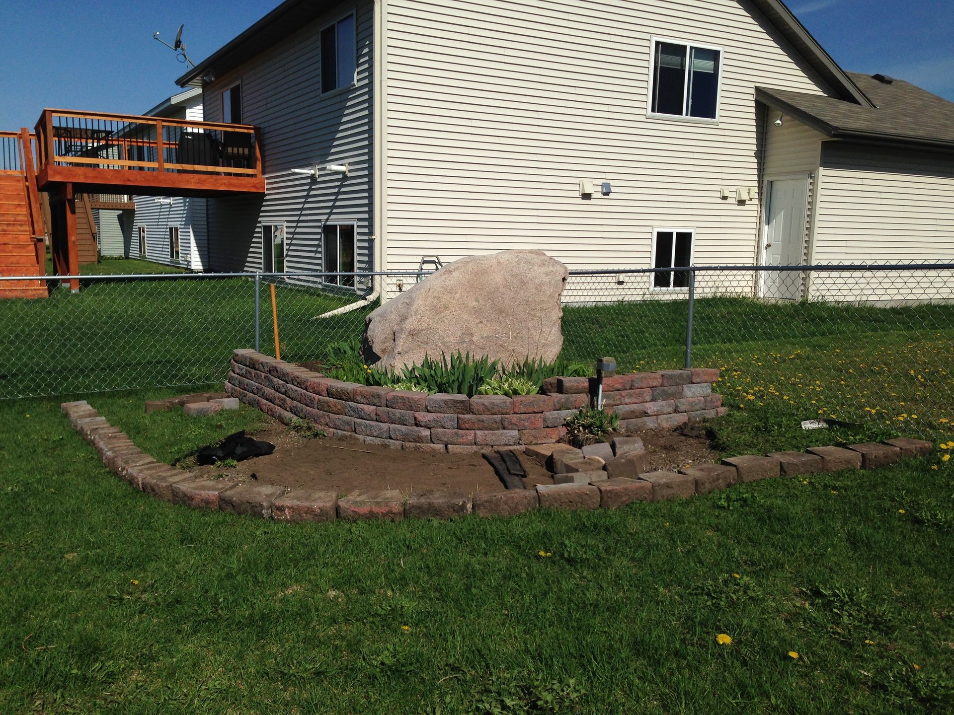 Completed outdoor fire pit with stacked brick retaining wall and decorative stone feature in residential backyard.