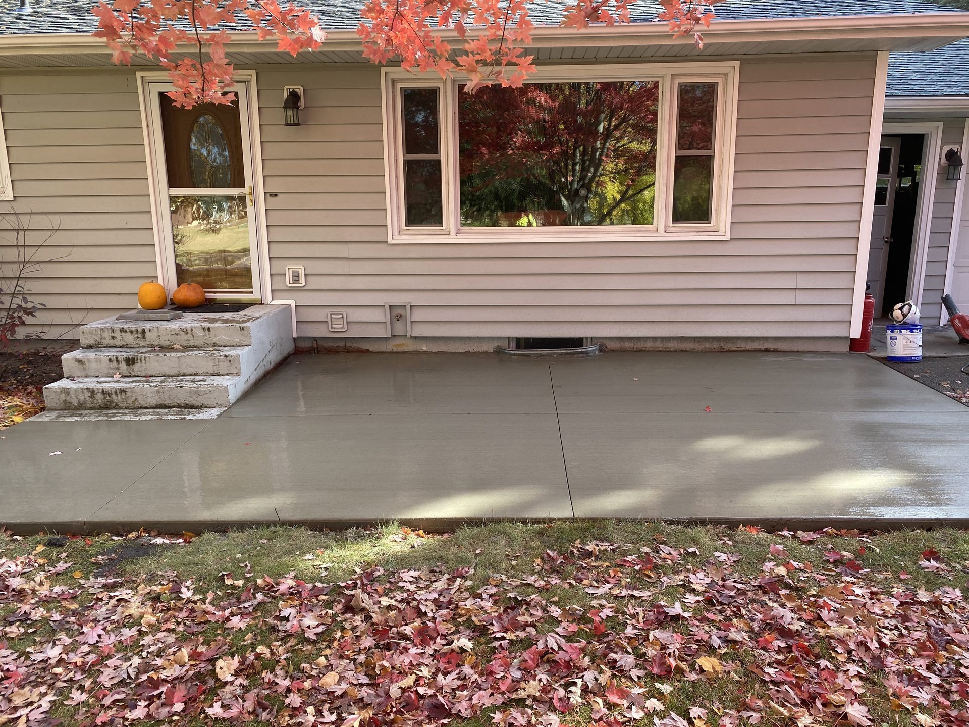 Newly finished concrete driveway with clean edges and smooth surface, fronting a mauve-colored residential home with fall foliage in background.