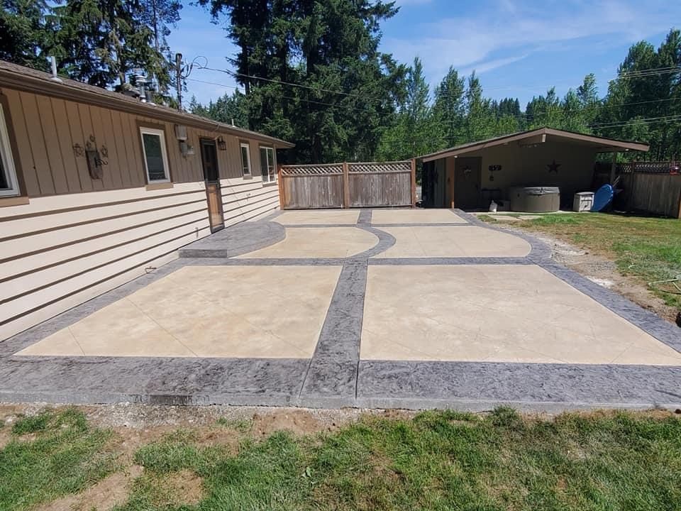 Finished concrete patio with decorative gray borders and circular design elements, residential property with attached garage and carport.