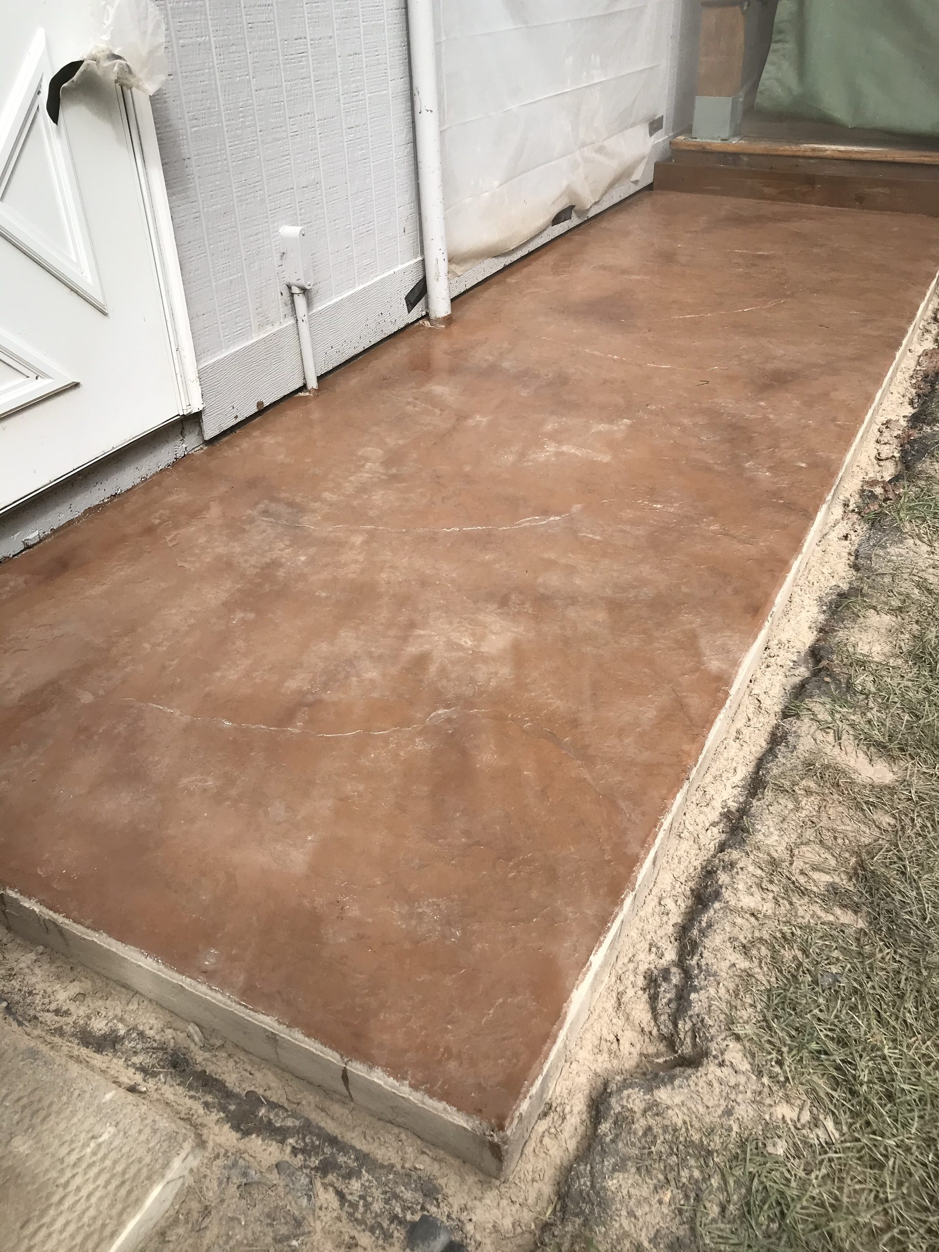Newly finished concrete pad with smooth brown surface and clean edges, adjacent to residential structure and landscaping.