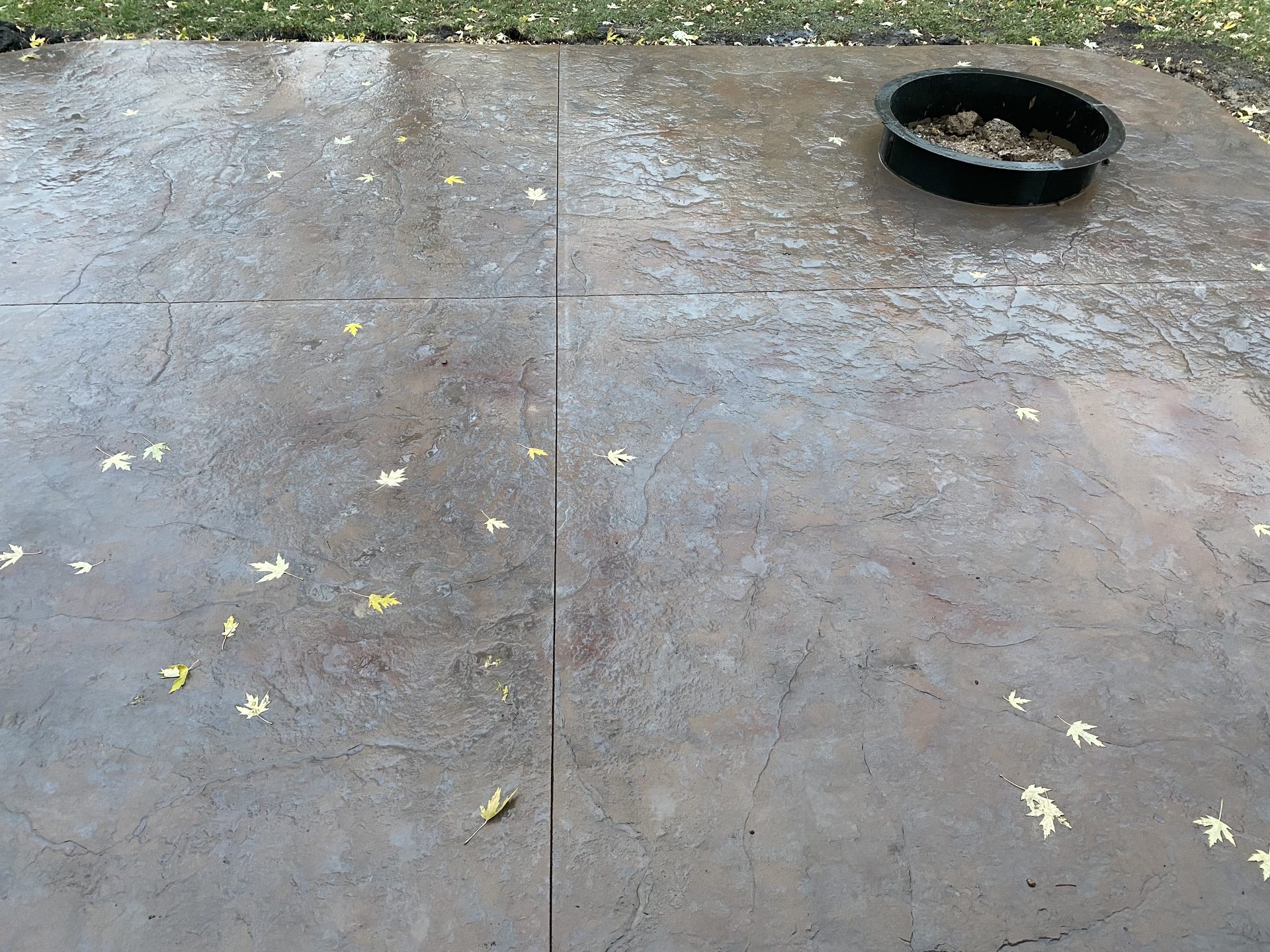 Finished concrete patio with control joints and a black debris basin, scattered autumn leaves visible.