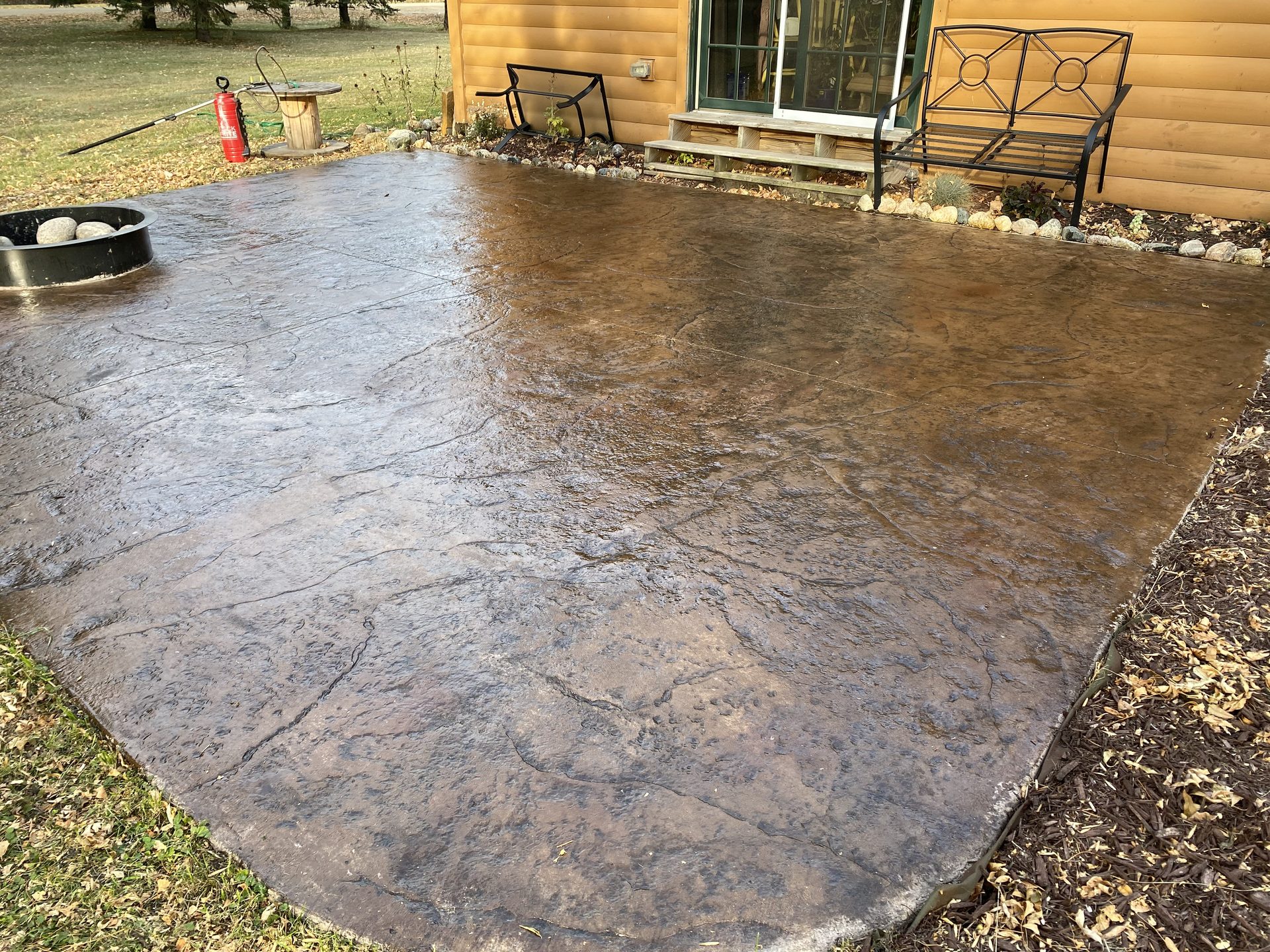 Completed stamped concrete patio with earth-tone finish installed beside residential cabin.