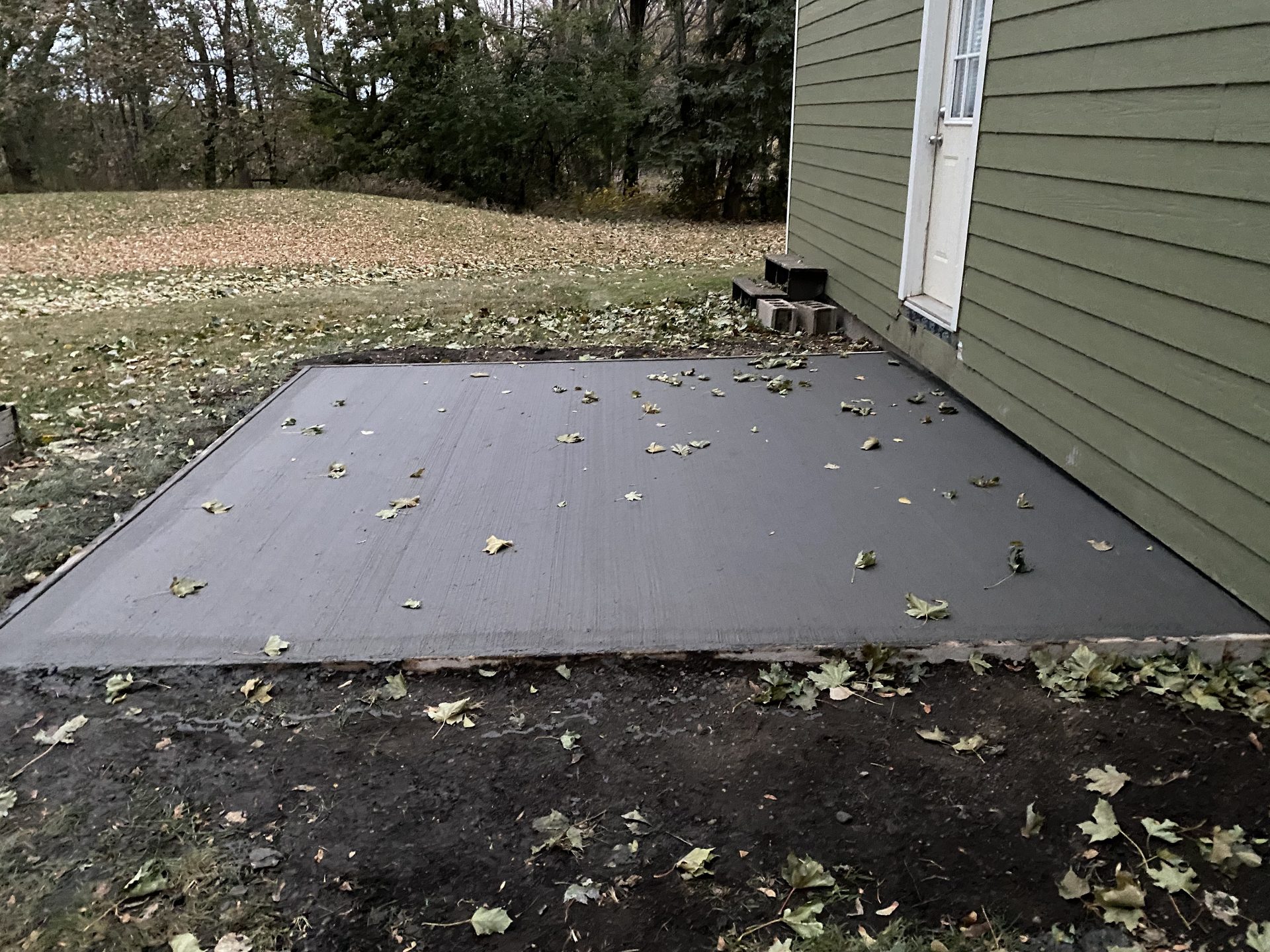 Newly installed composite deck adjacent to house siding with autumn leaves scattered across the surface and surrounding yard.