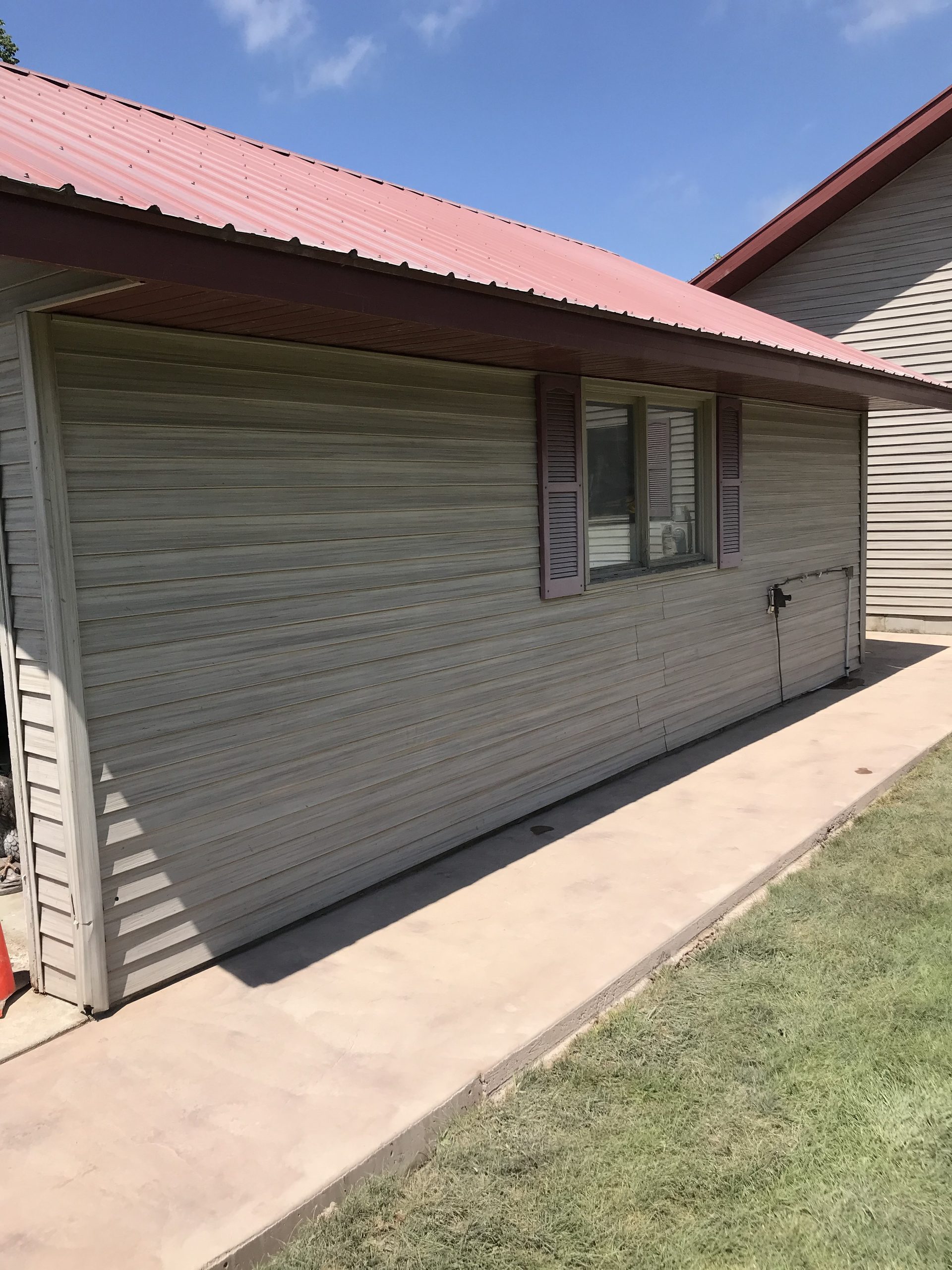 New gray metal siding garage addition with red metal roof and garage door, connected to residential home.