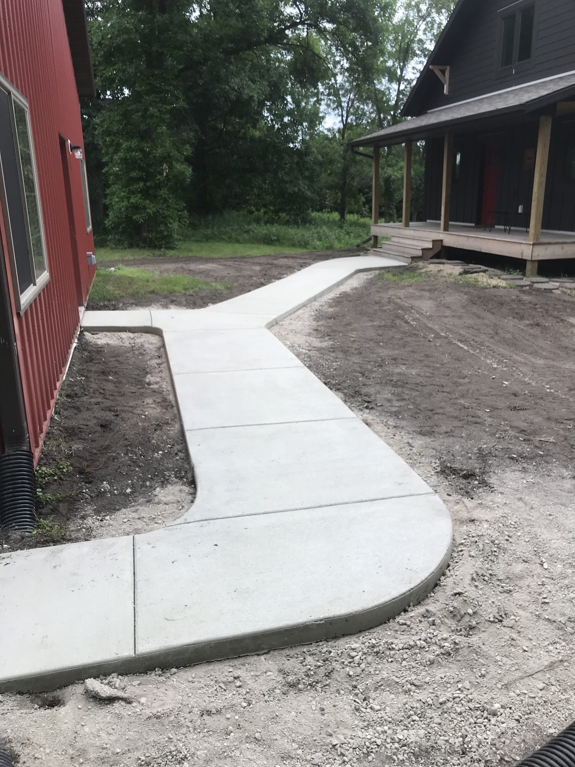 Freshly poured concrete pathway in an excavated trench, showing clean gray finish with white edge forms along the sides.