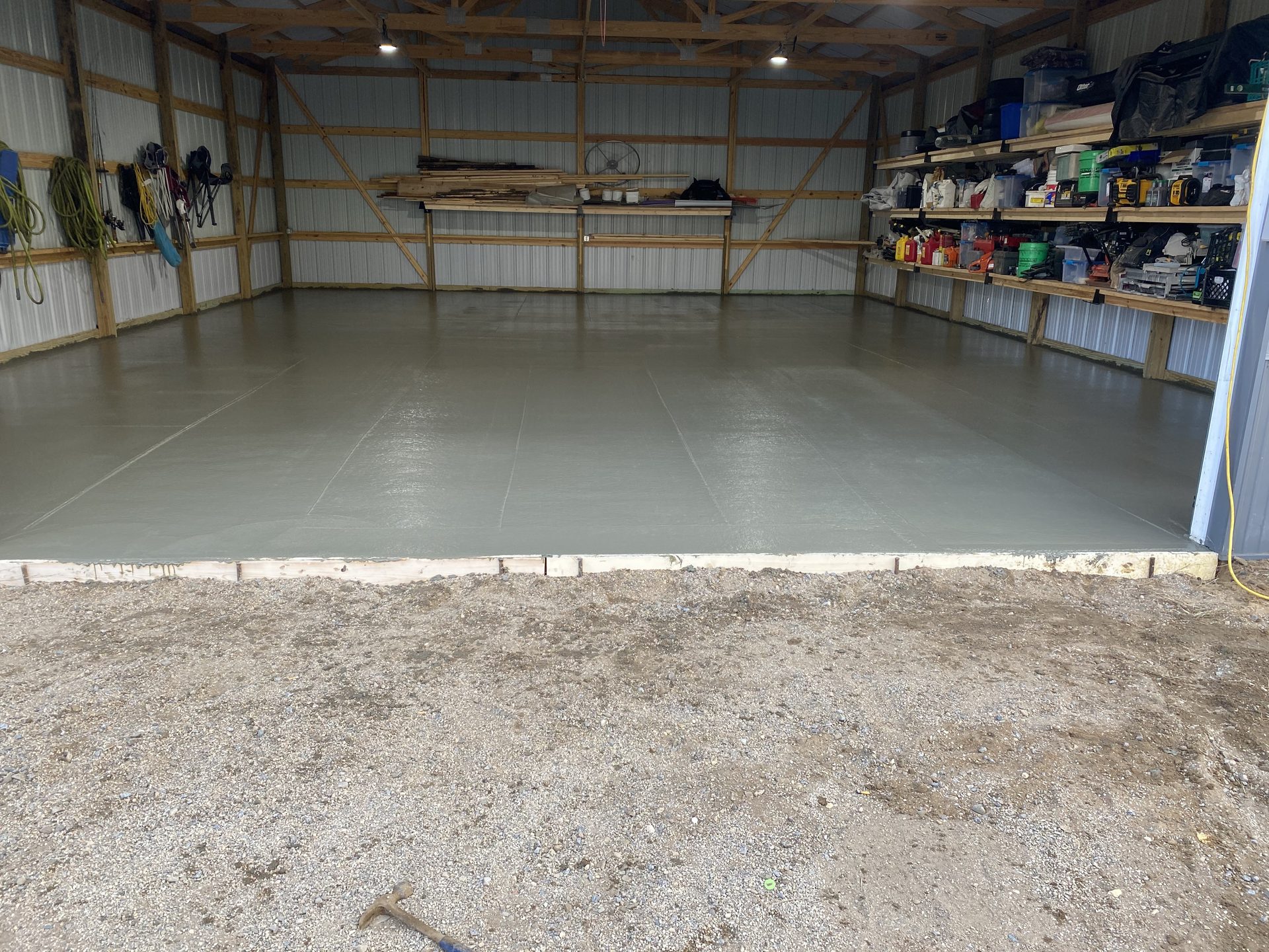Finished concrete garage floor in a metal-frame building with wooden shelving and storage along the walls.