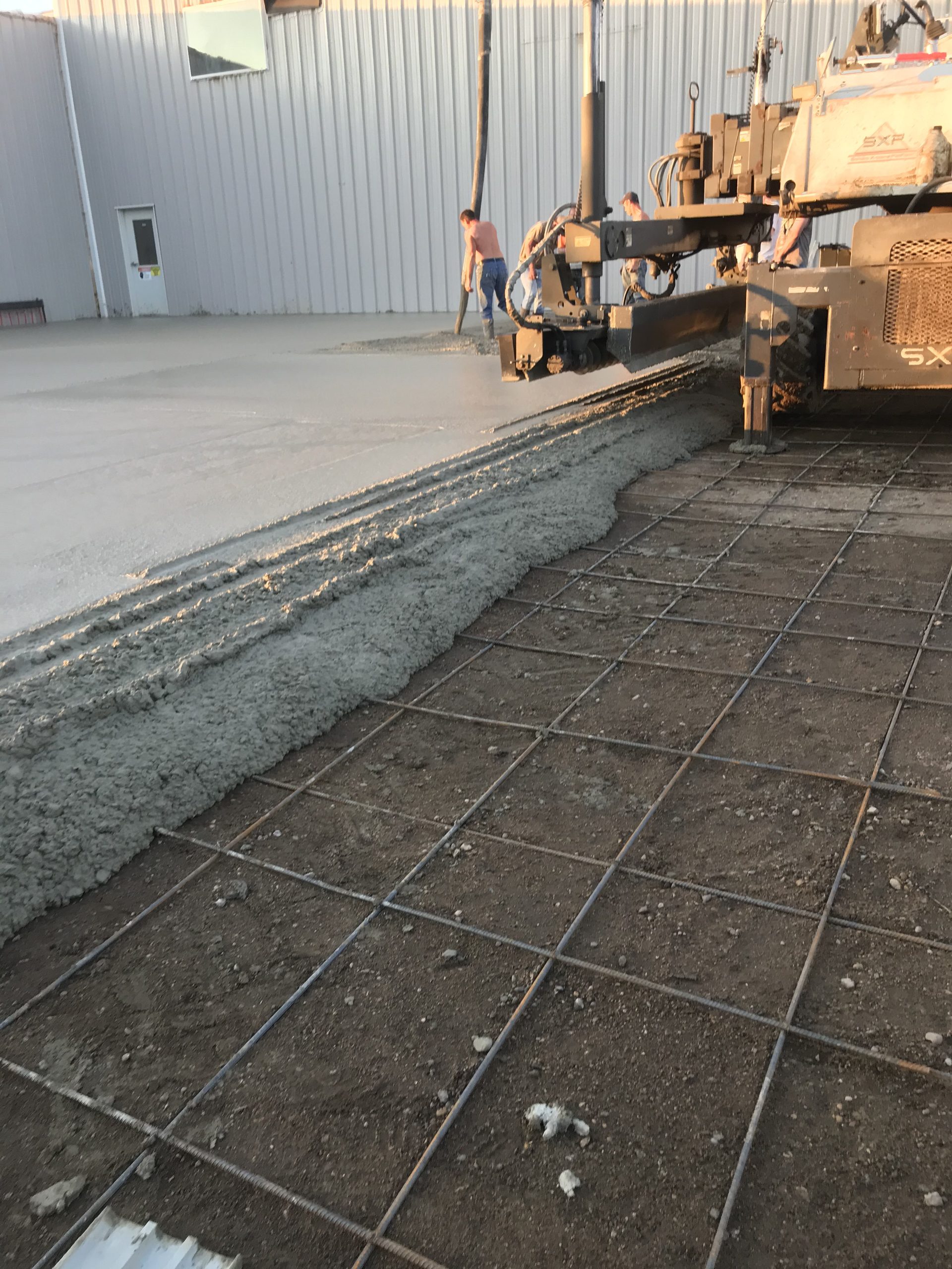 Concrete foundation pour in progress with rebar grid laid out on prepared subgrade, showing fresh concrete edge and equipment on jobsite.