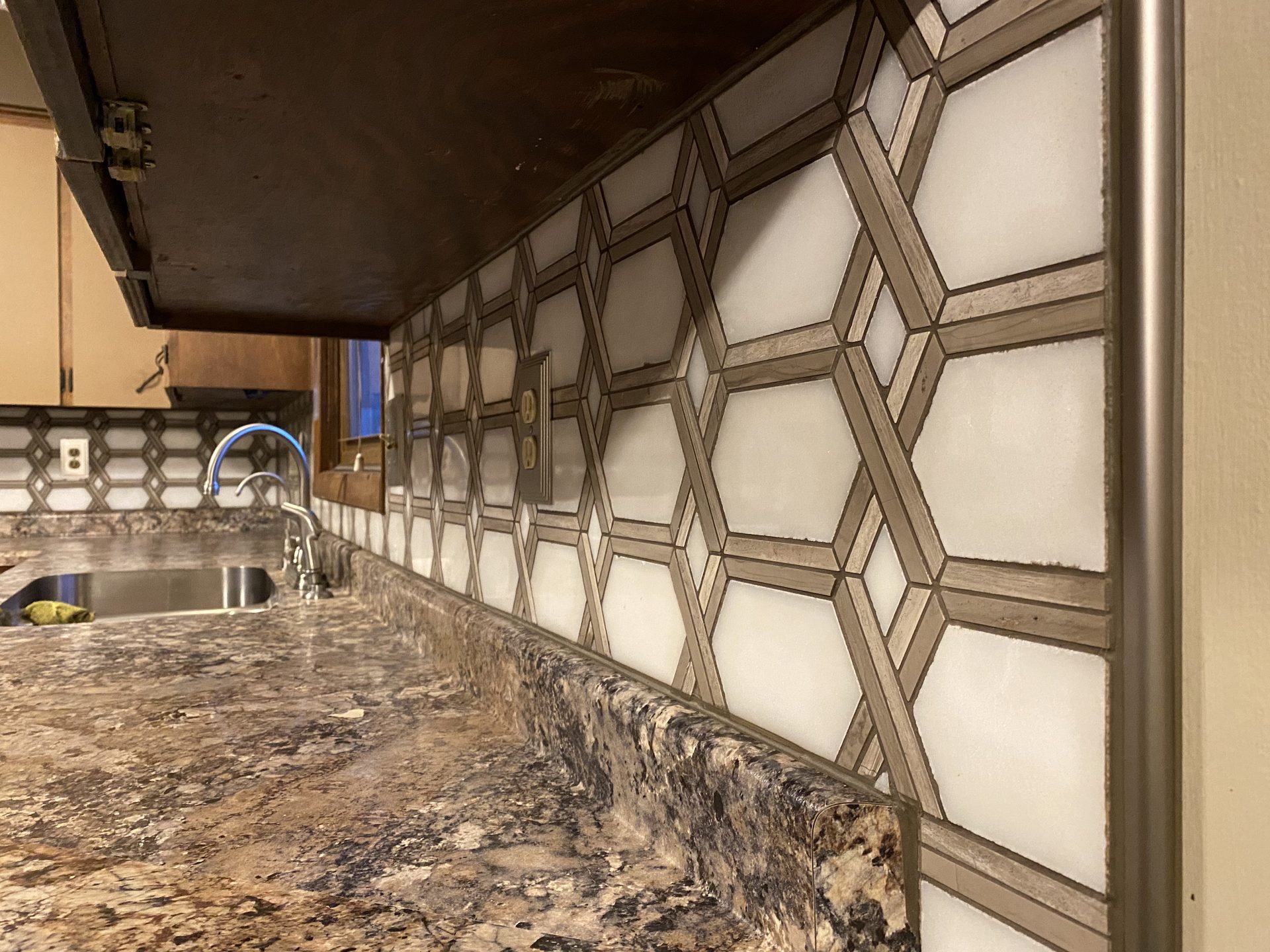 Modern kitchen with geometric wood-frame cabinet fronts, granite countertop, and stainless steel sink fixtures.