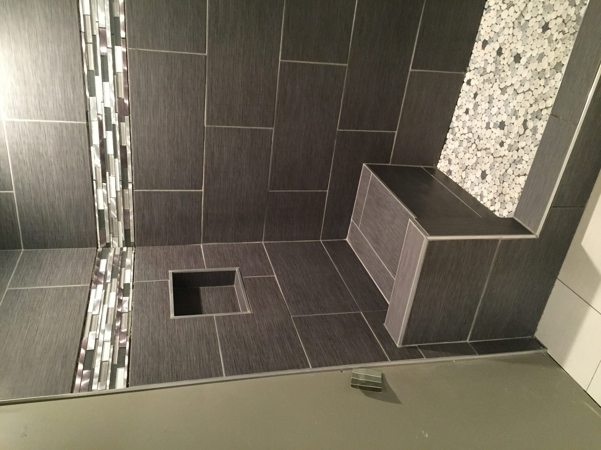 Completed tile shower featuring white herringbone subway tile walls and two hexagonal tile niches with black trim.