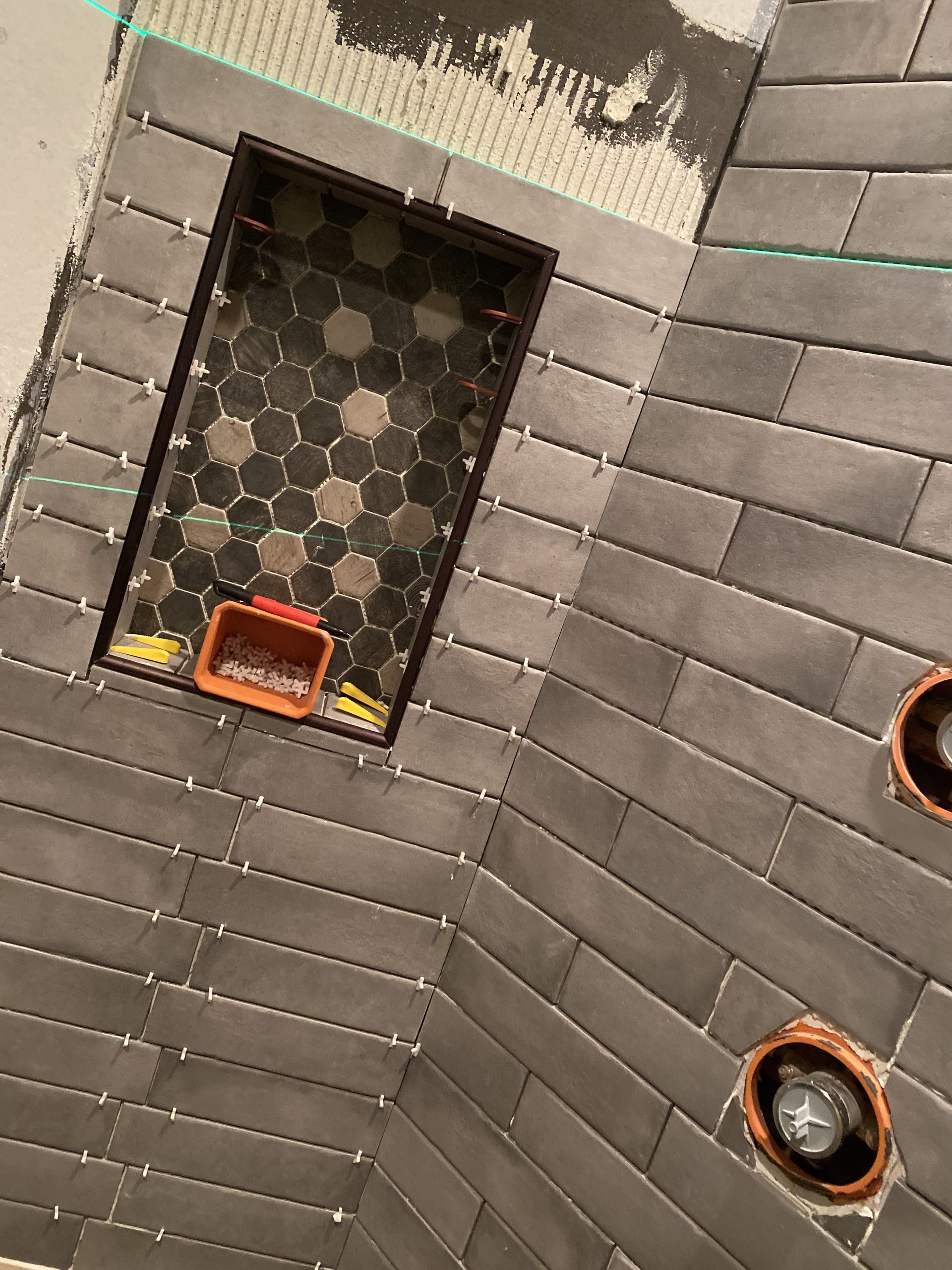 Subway tile shower installation in progress showing white ceramic tiles, plumbing rough-in, and shower valve fixture.