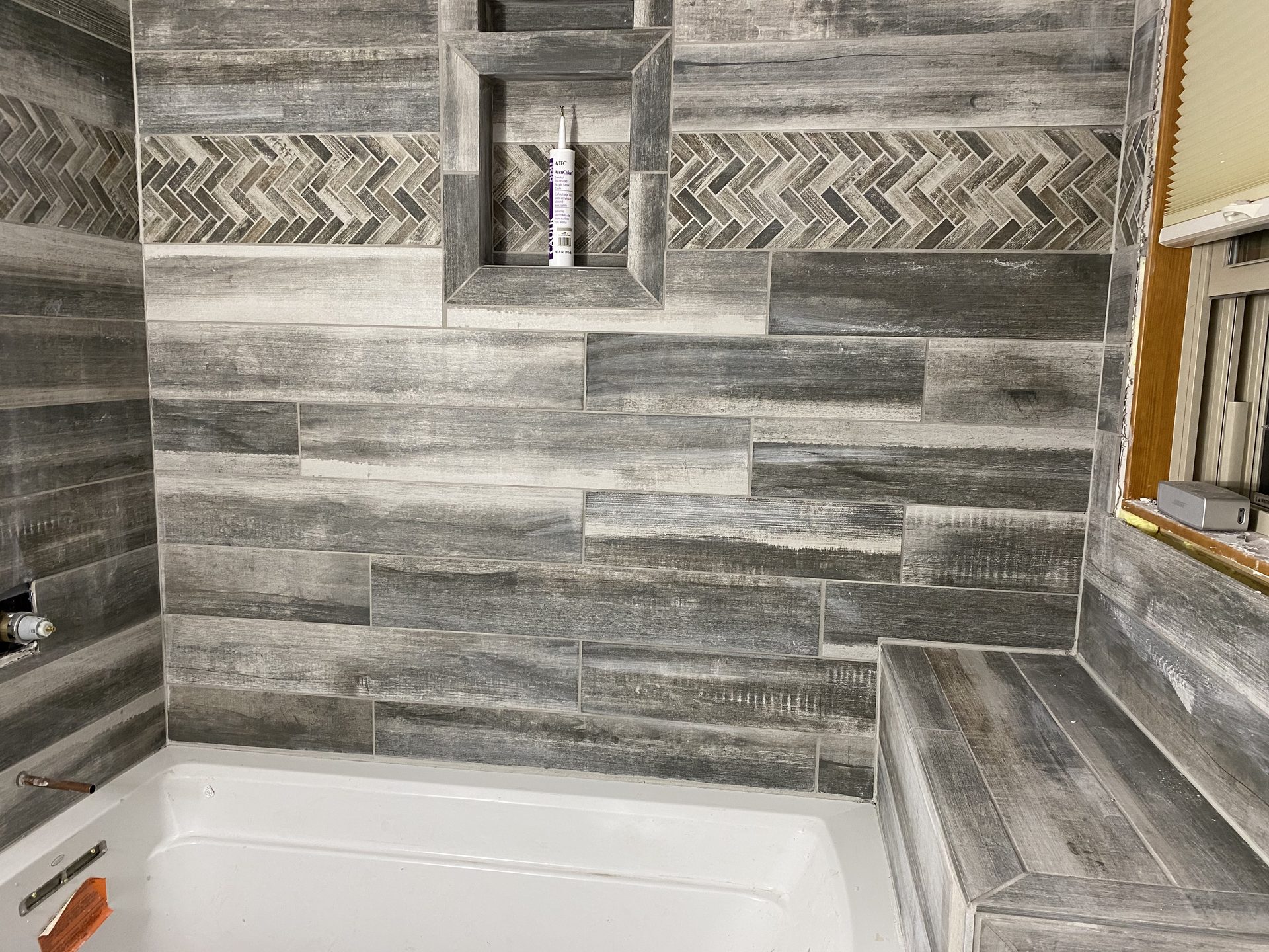 Marble subway tile shower surround with white bathtub and polished chrome trim.