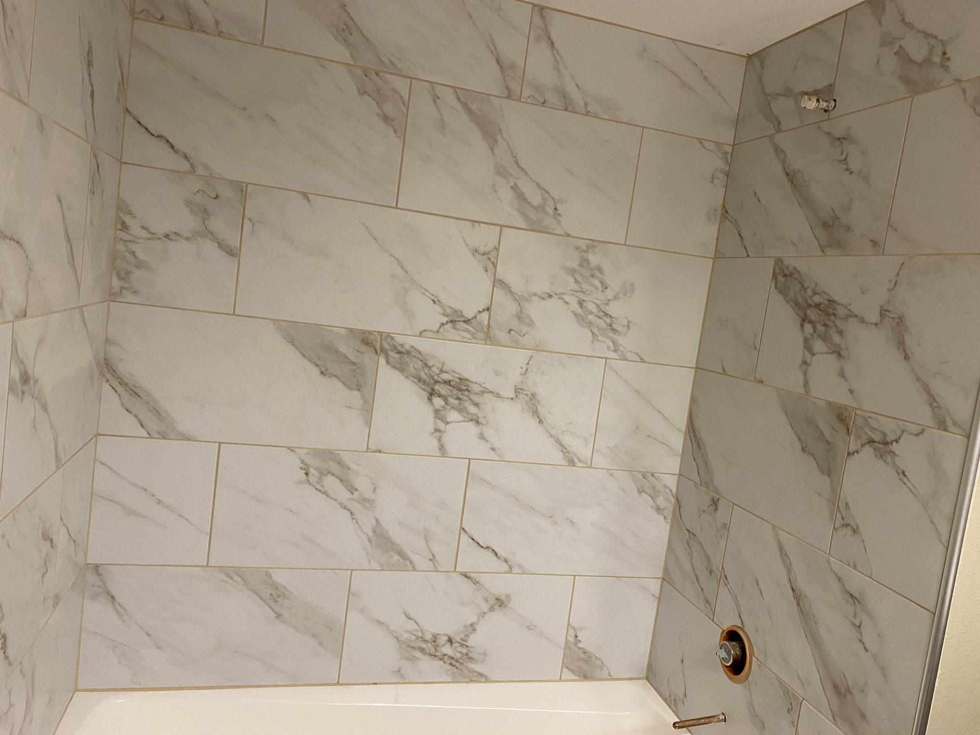 Marble tile shower surround with subway-style layout and taupe veining throughout three walls.