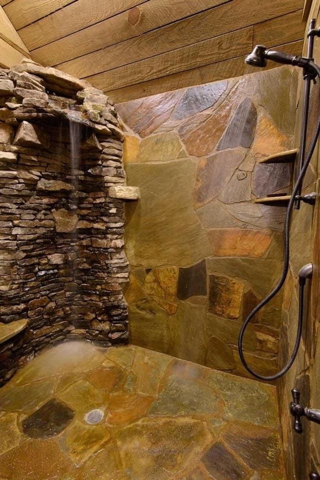 Completed natural stone shower with stacked stone wall feature and slate tile surround, wooden beam ceiling visible.